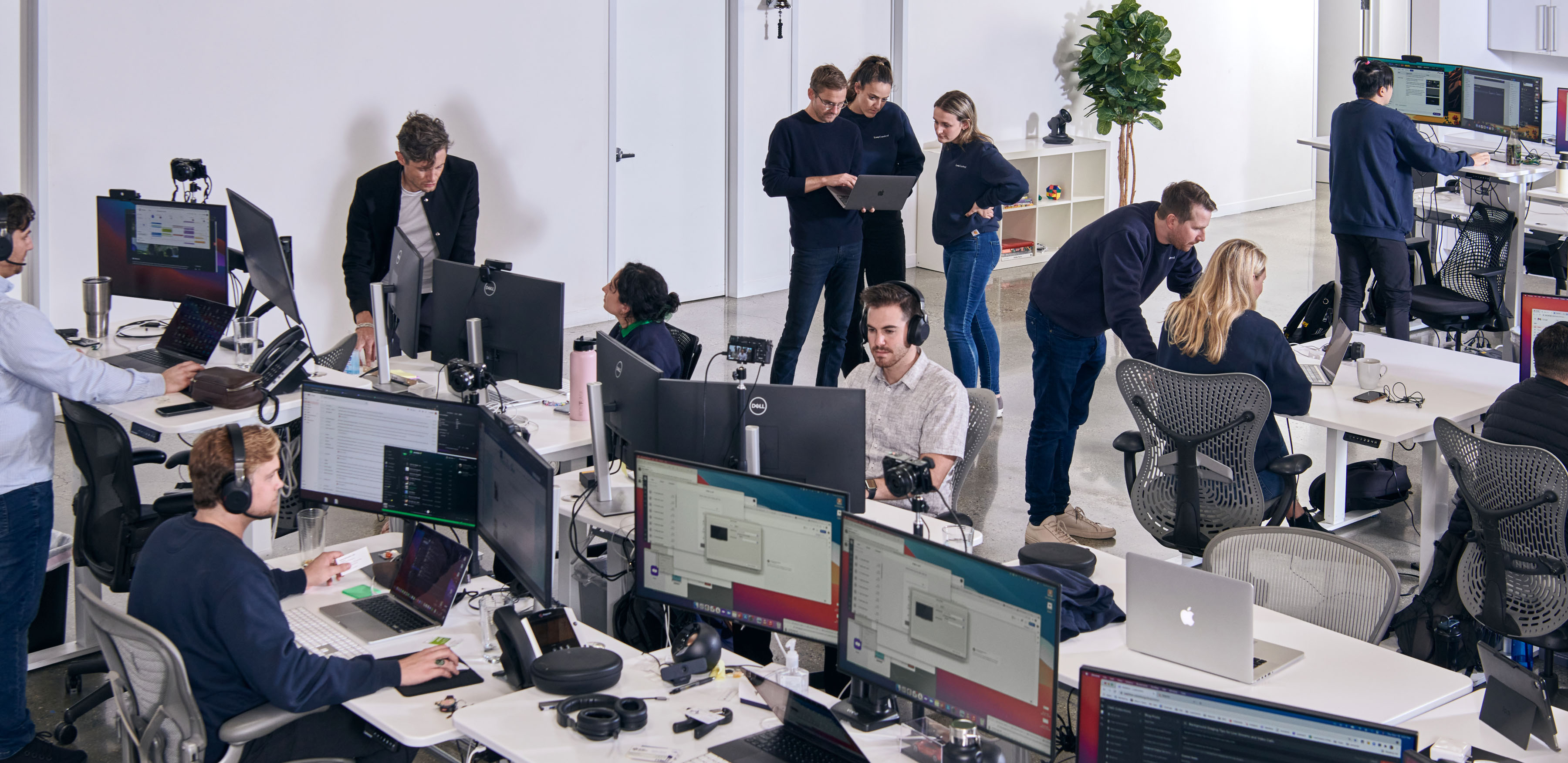 A large office with 3 groups of people collaborating and several others working at their desks.