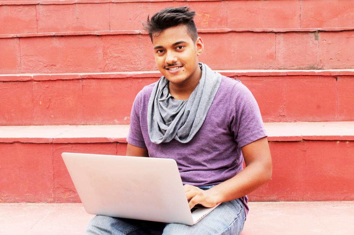 Student with a laptop perched on their knees smiles at the camera.