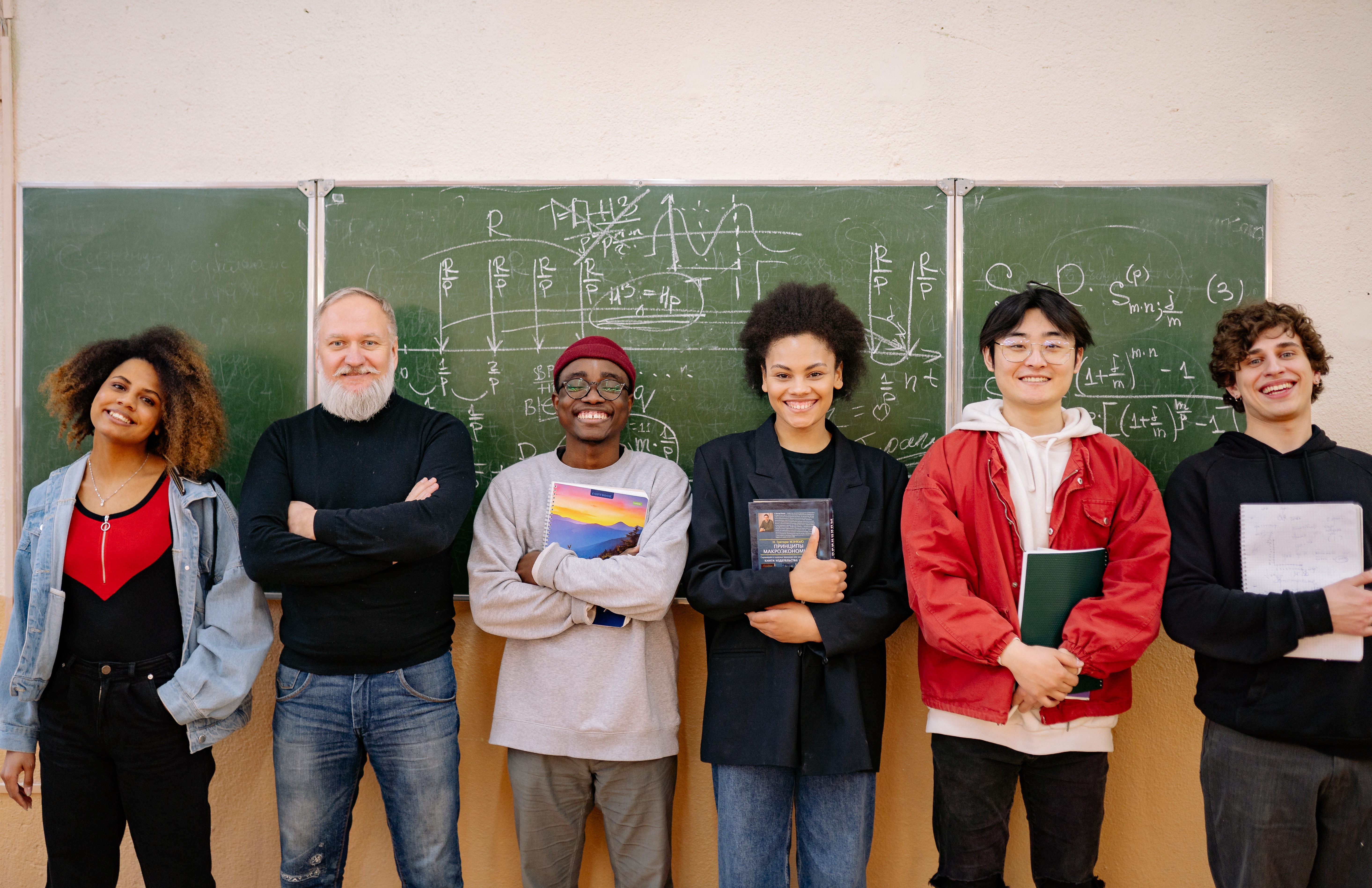 A diverse group of students and teachers stand in front of a chalkboard covered in math equations