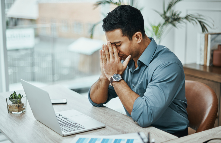 Person at table with a laptop open and their head in their hands