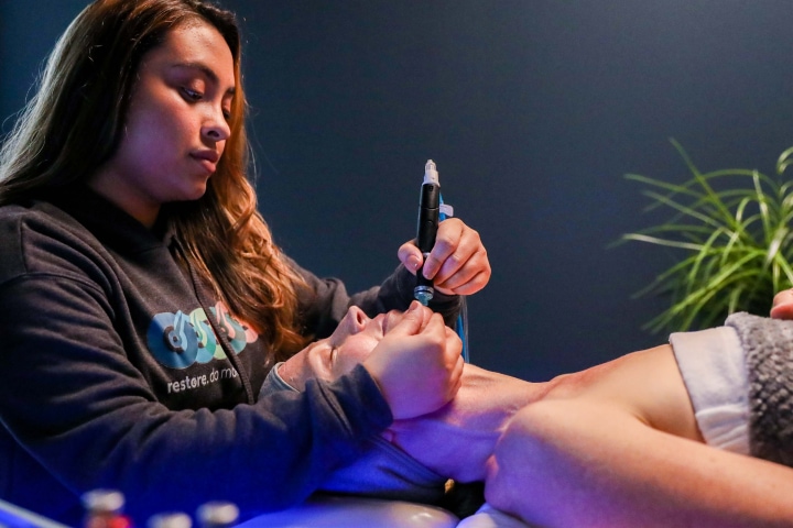 Woman laying on back with esthetician performing hydrafacial.