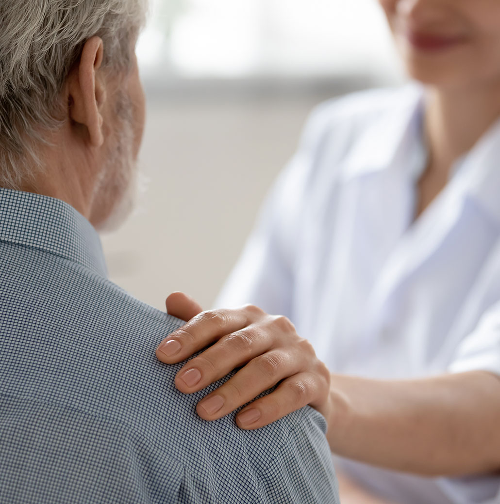 close up of nurse with hand on older males shoulder