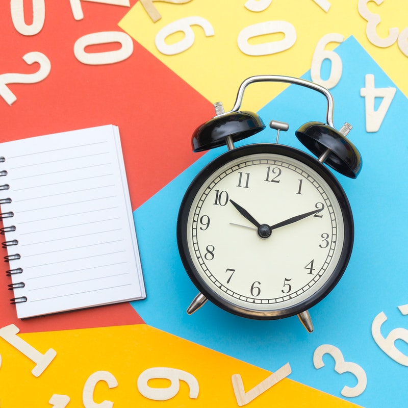 Old-fashioned black alarm clock on table next to blank white notebook