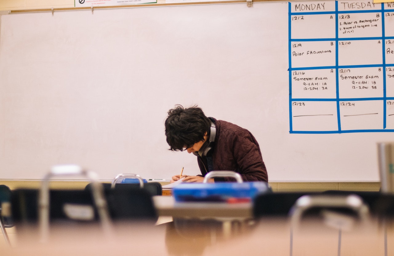 Photo of a student in a brown sweater sitting down in a classroom and taking the easiest standardized test for college