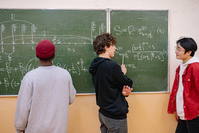 three male students writing on chalkboard