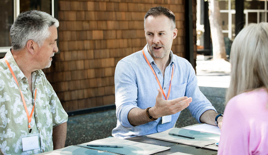 Three teachers, sitting at a table outside, talking and looking at Wayfinder workbooks.