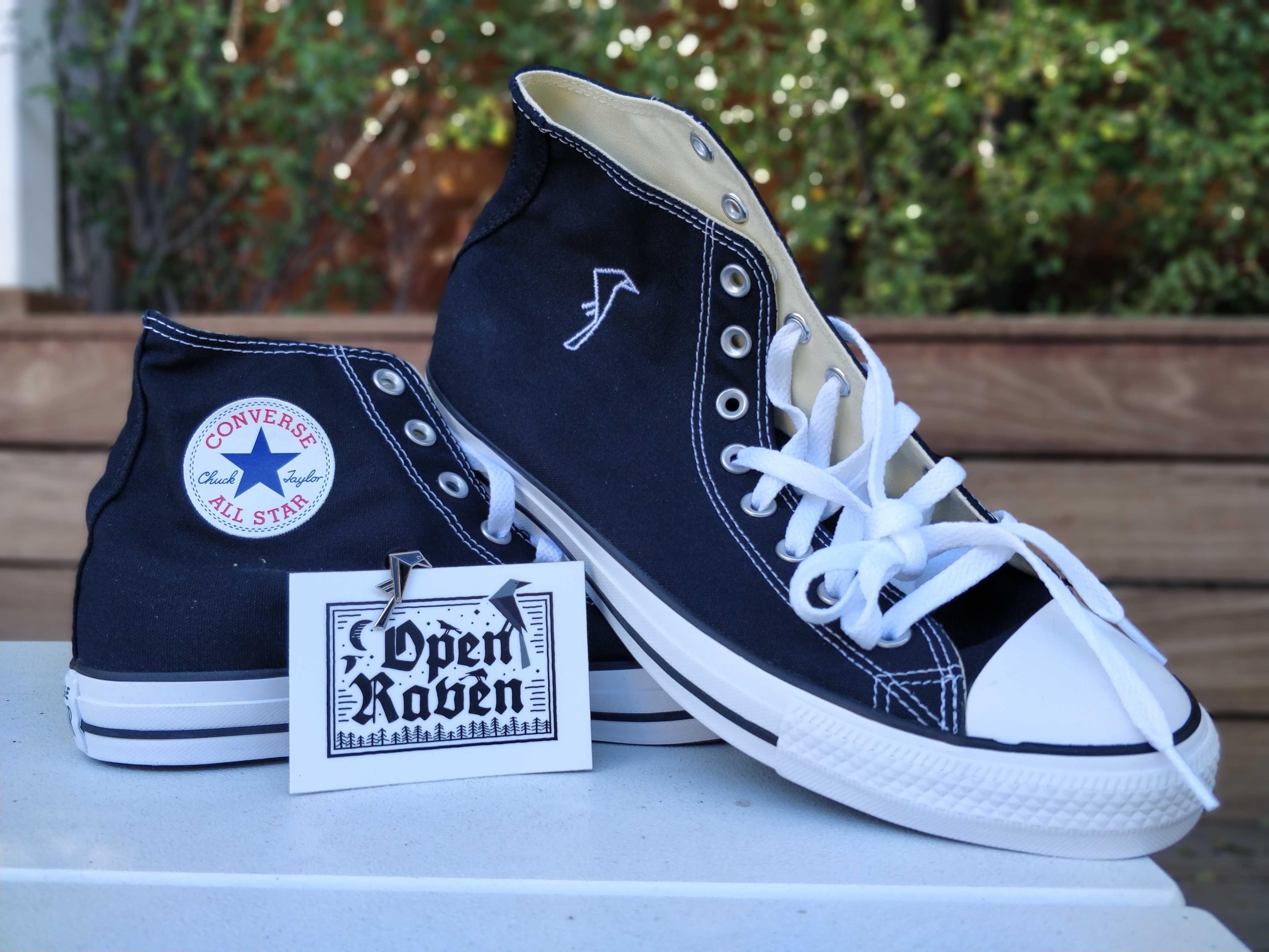 Black Converse with Open Raven logo with an Open Raven sticker and enamel Open Raven pin propped up against the shoes