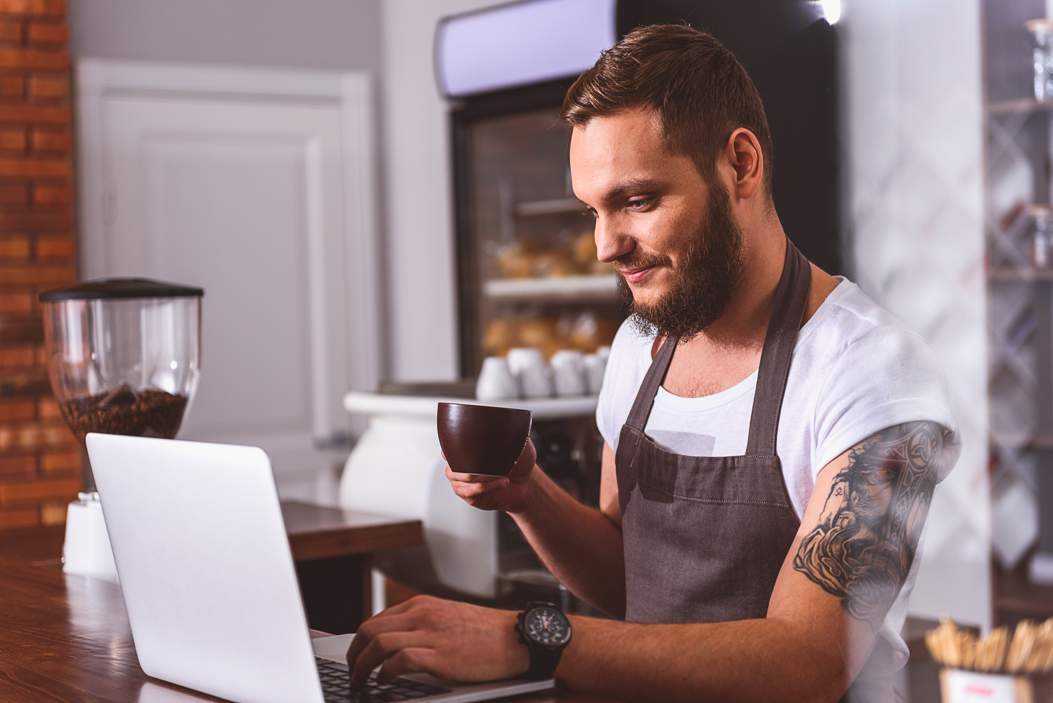 Barista drinking a coffee looking at a laptop