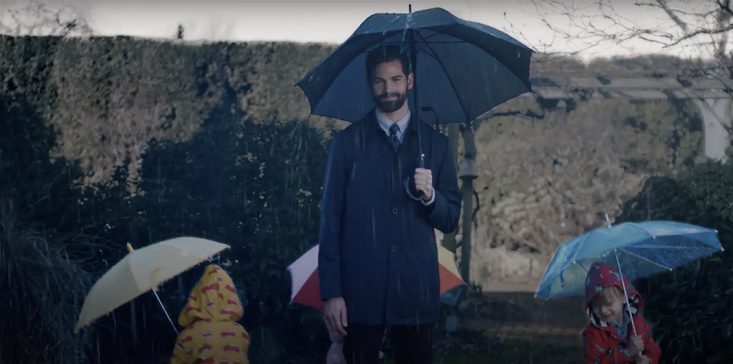 A man in a suit standing in the rain with an umbrella.