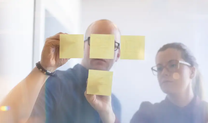 Amanda and Rory deep in focus with branding strategy and web design with post it notes on a glass board.