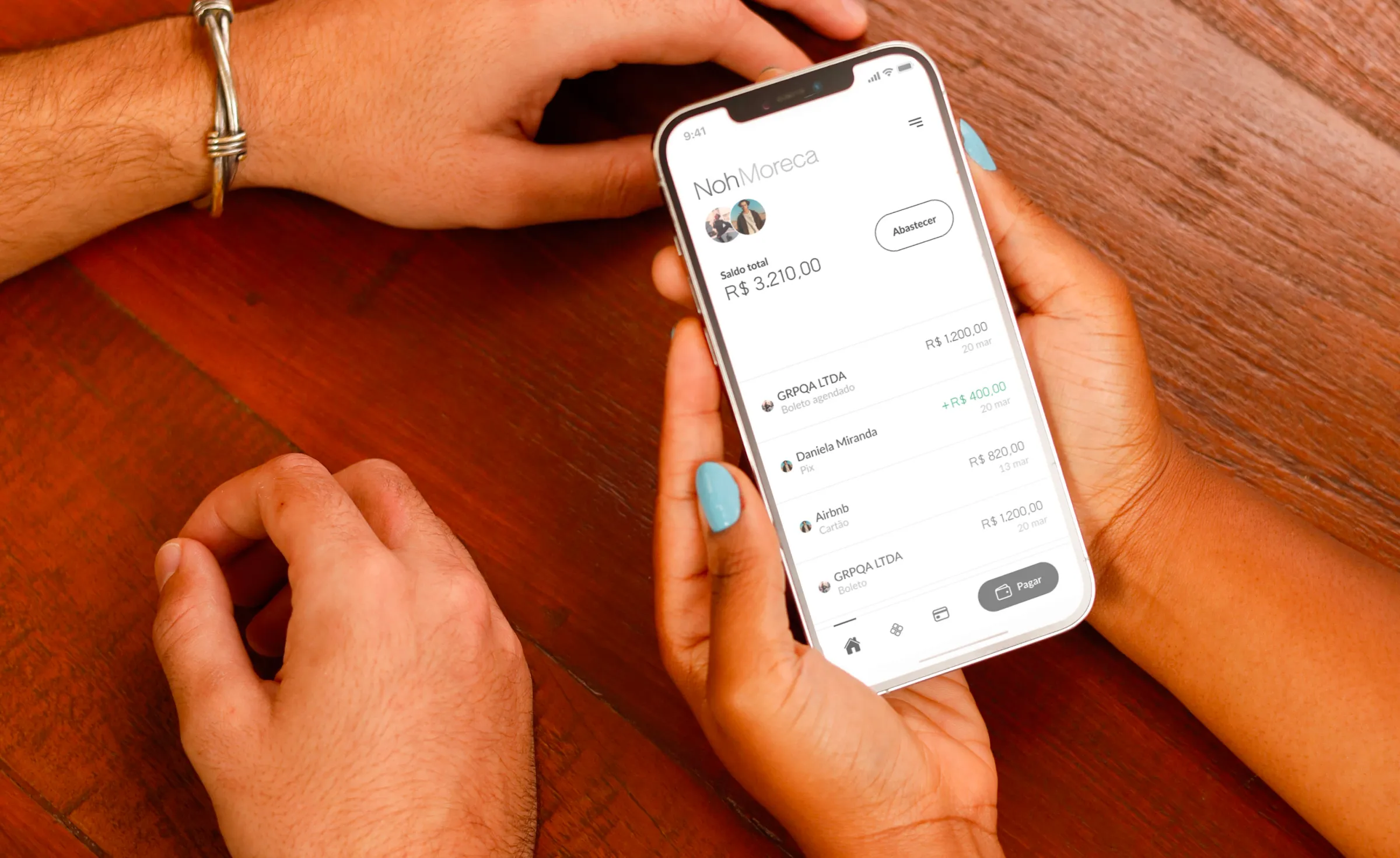 Uma esposa segurando celular com aplicativo Noh aberto enquanto o marido fica ao lado.