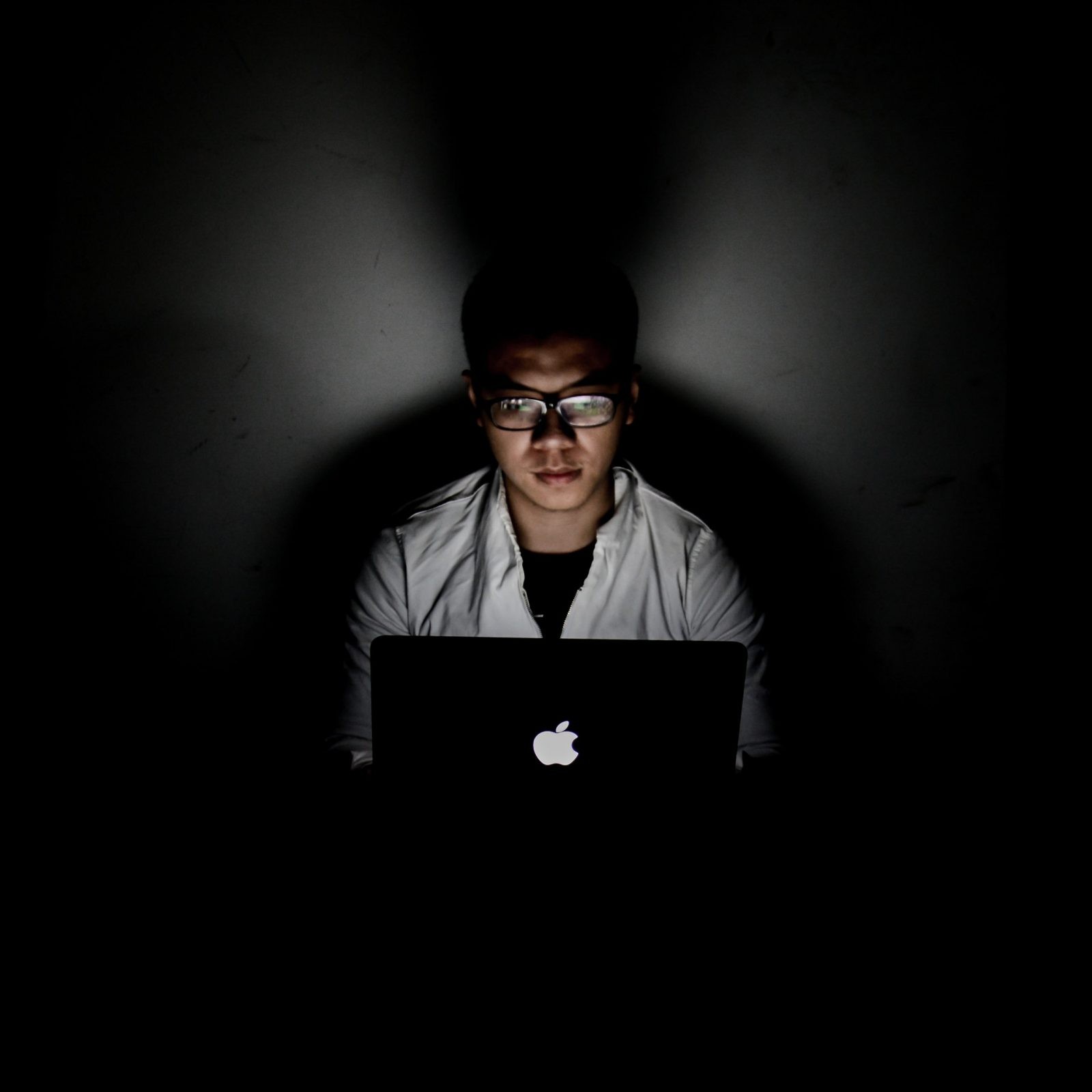 a-guy-looking-at-his-computer-in-a-dark-room-with-a-black-wall