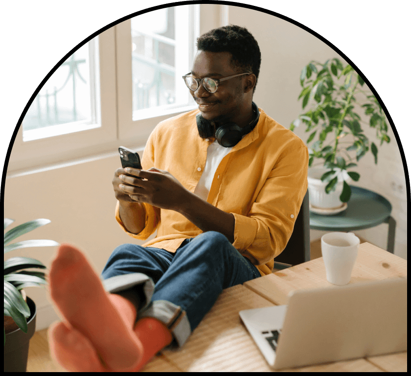 African american man in a goldenrod shirt sitting and smiling at his phone