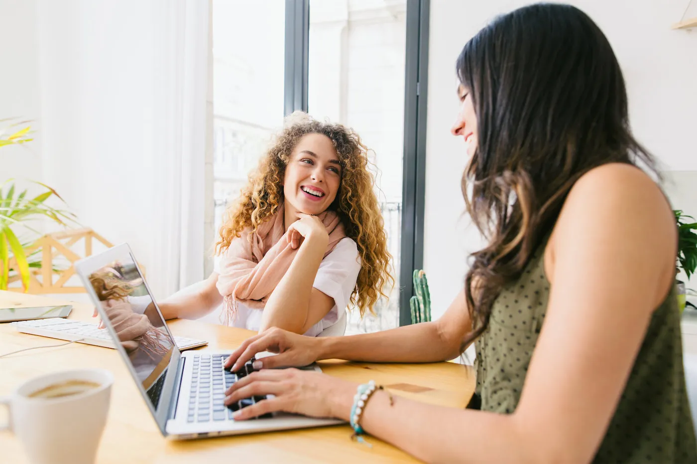 Two woman smiling at each other while one types on a laptop
