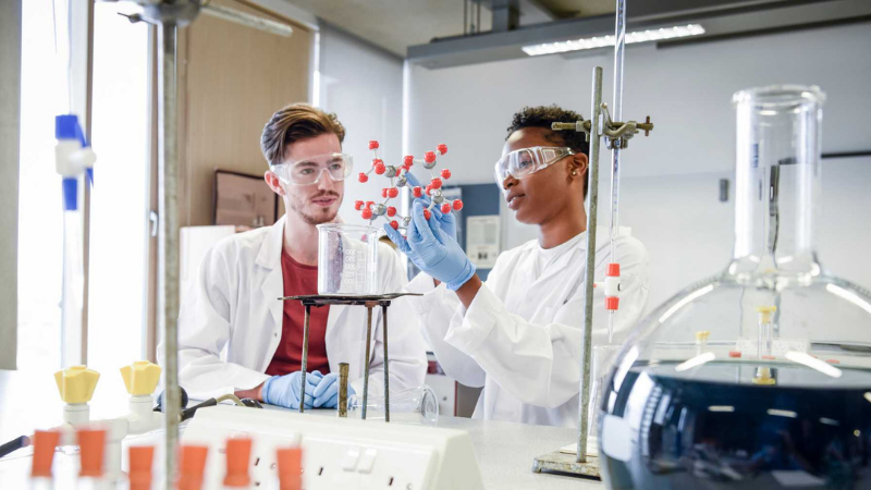 Male and female science students using equipment and watching liquid in beaker