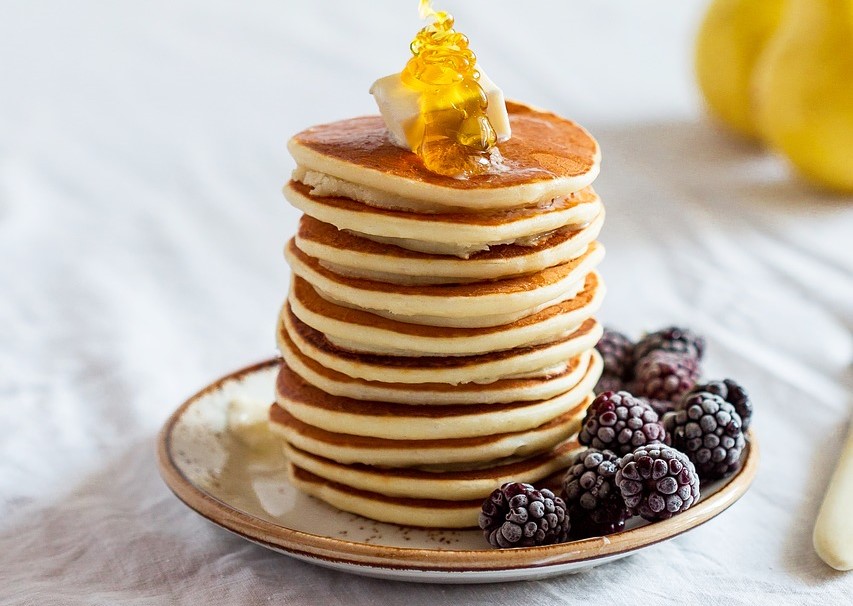 Ein Turm aus gesunden Pancakes auf einem Teller wird mit Honig begossen.