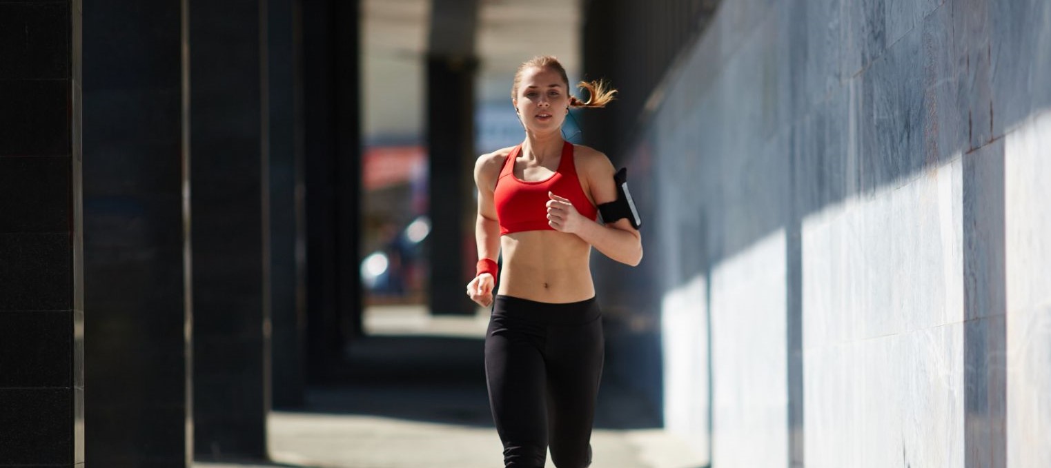 Eine Frau in Trainingskleidung joggt auf einer Brücke. 