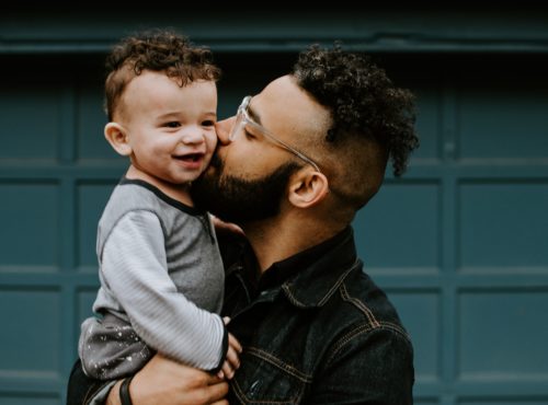 A dad kisses his toddler on the cheek.