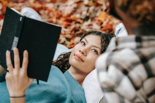 Person lies on the ground reading a book and smiling.