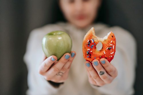 Close-up of a person's hands holding an apple and a doughnut with a bite taken out of it.