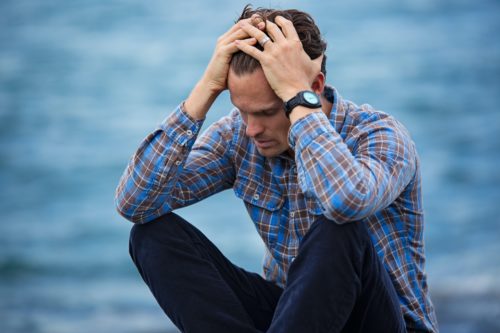 A worried person sits on the ground with their head in their hands.