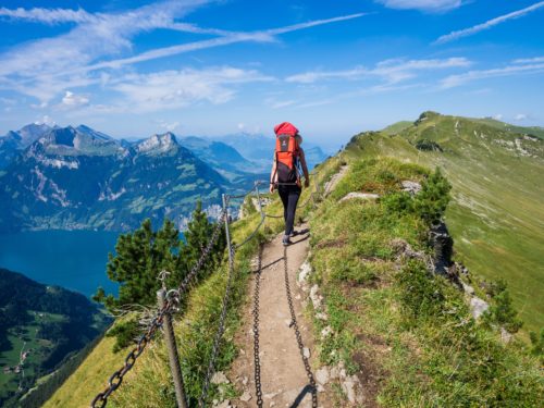 Person wearing a big red backpack walks along a trail on a mountain ridge.