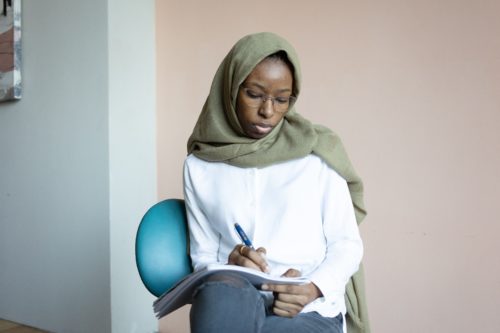 A person sits in a chair writing in a notebook.