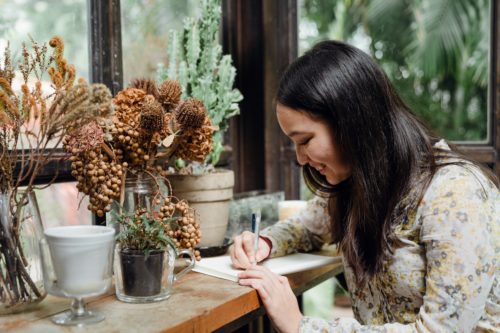 A writer scribbling in a notebook at a wooden table.