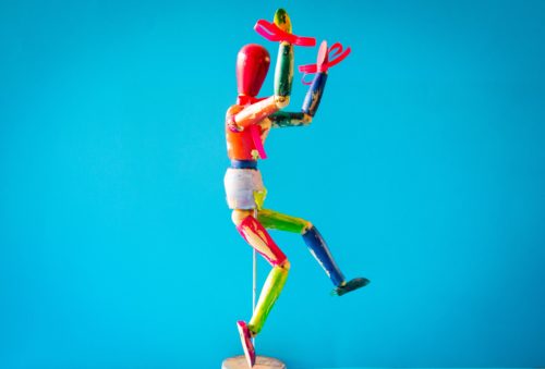A wooden drawing model painted, decorated, and posed as a playful jester archetype.