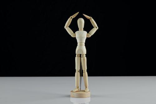 A drawing figure positioned with its arms over its head against a black background.