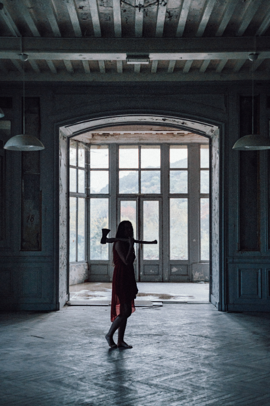a woman in a dress holding an axe in an abandoned house.