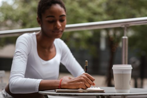 A woman writing in a notebook at a table outside.