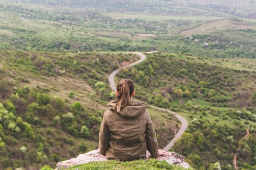 A person sits on a hill overlooking a winding road.
