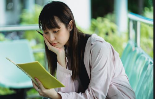 Person thinks while holding a pen and looking at a notebook.