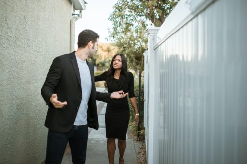 A couple argues on the walkway between a fence and a building..