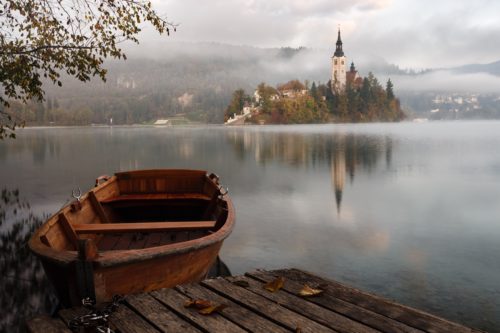 A misty fantasy landscape featuring a small rowboat at a wooden dock and a castle on an island in the distance.