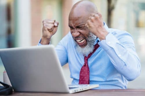 A bearded writer in a shirt and tie yells at a laptop computer.
