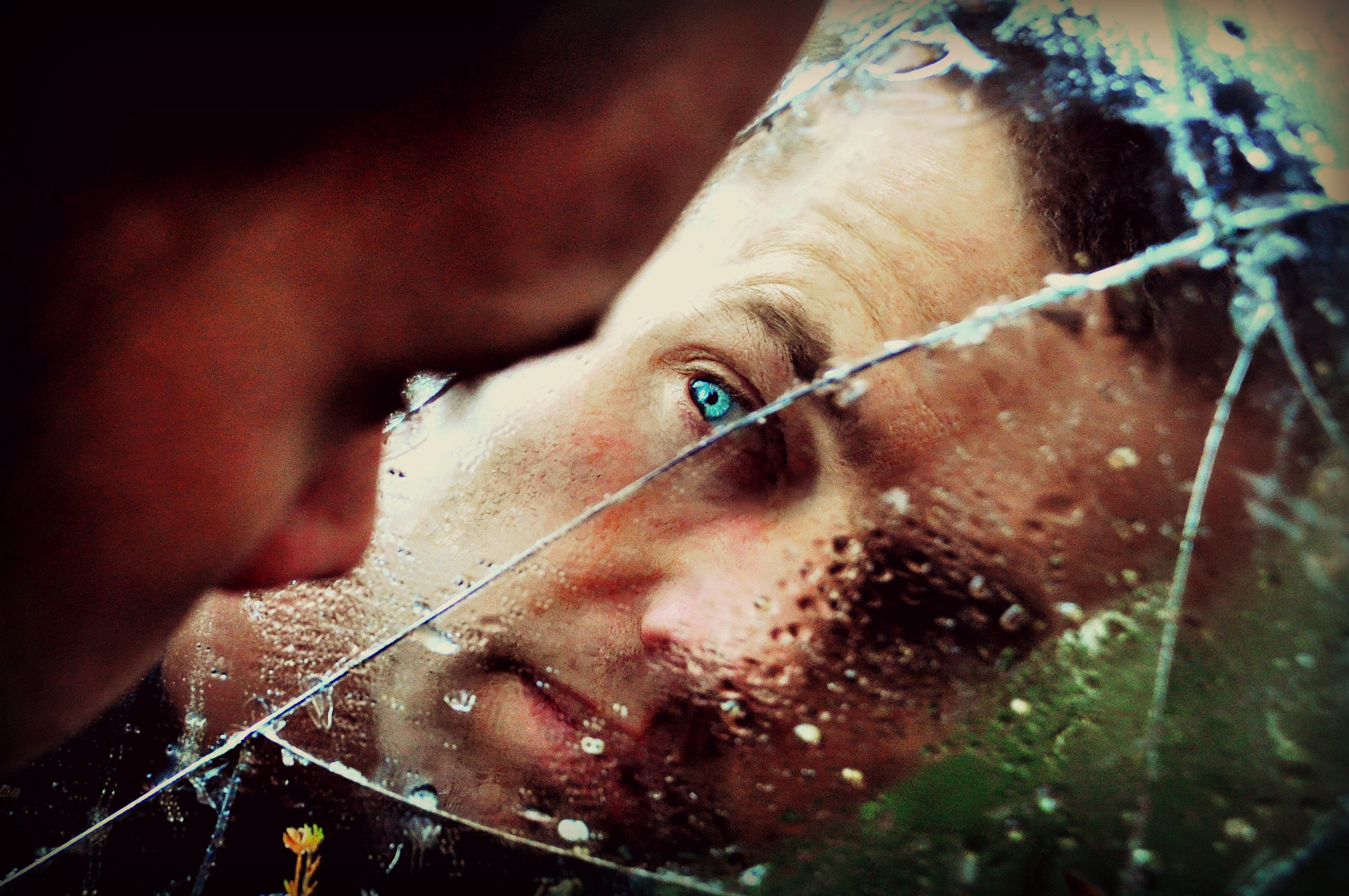 A man looking at his reflection in a cracked mirror.