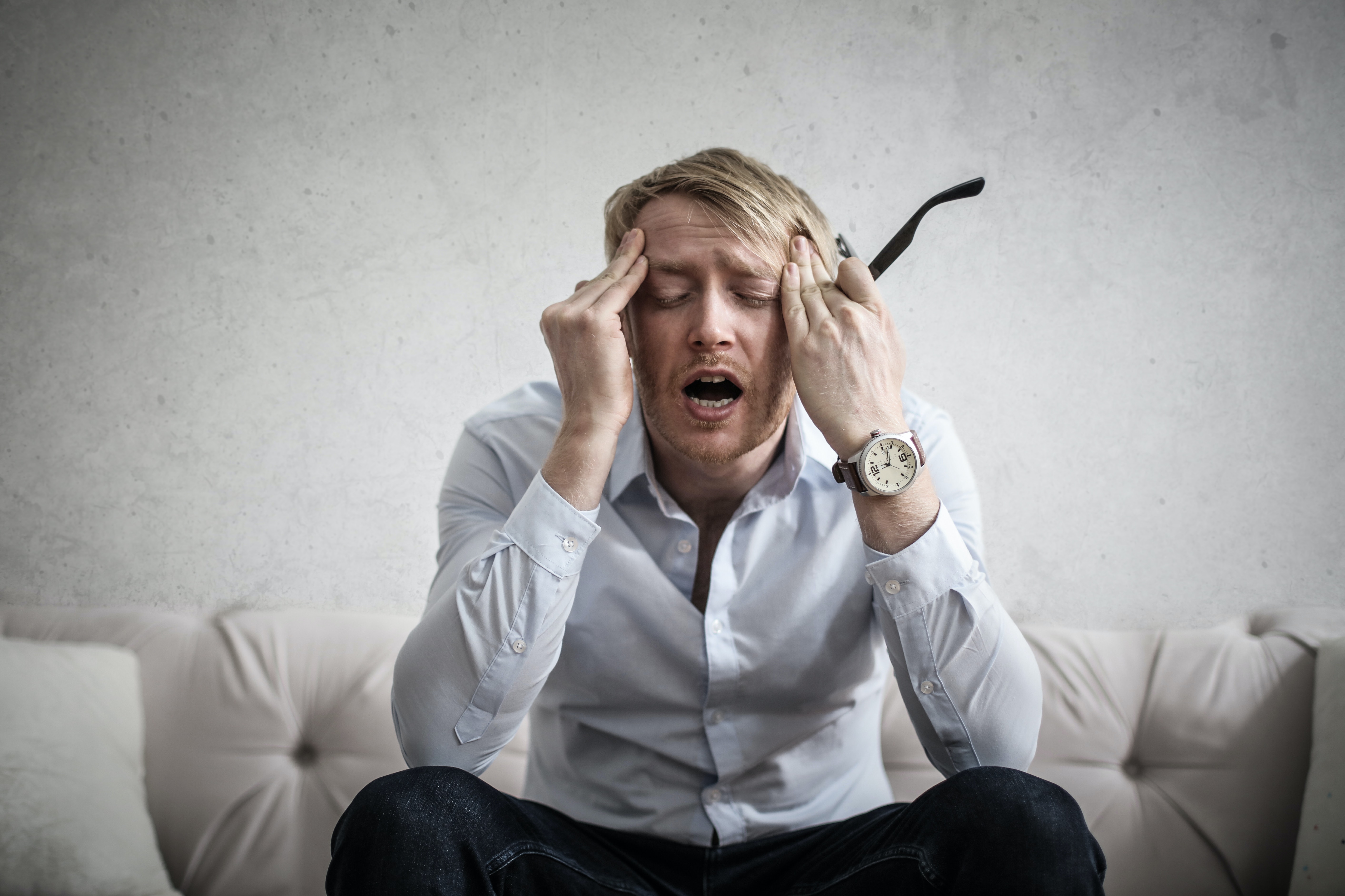 A stressed out man in a dress shirt and pants rubbing his temples.