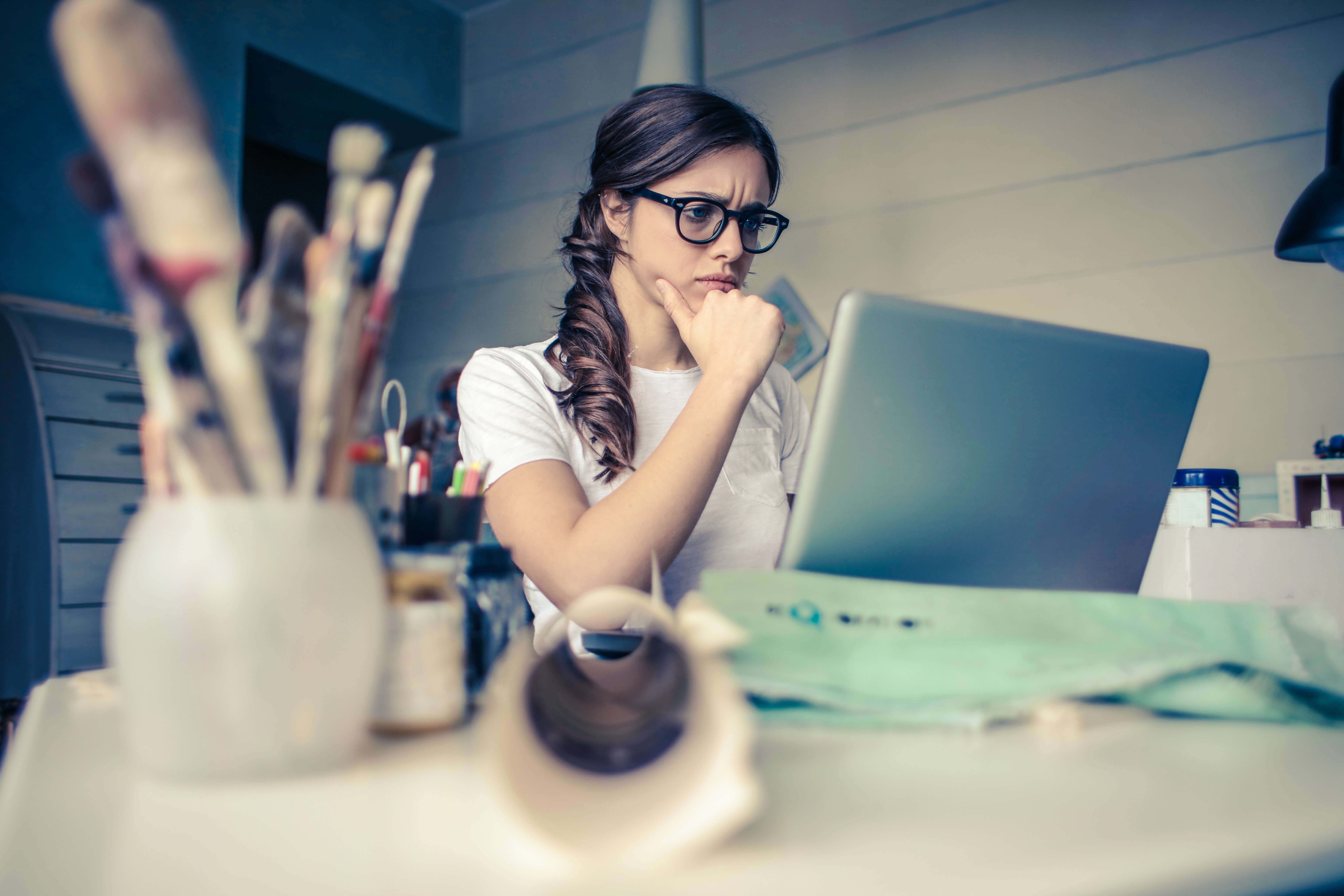 A person with long hair and glasses frowns at a computer screen.