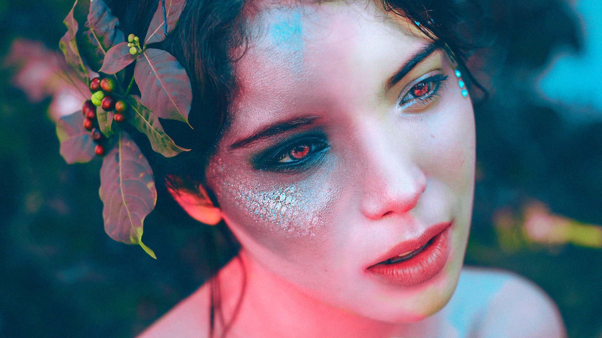 A fairy-like creature with red eyes, shimmering cheeks, and holly in her hair stares off into the distance.
