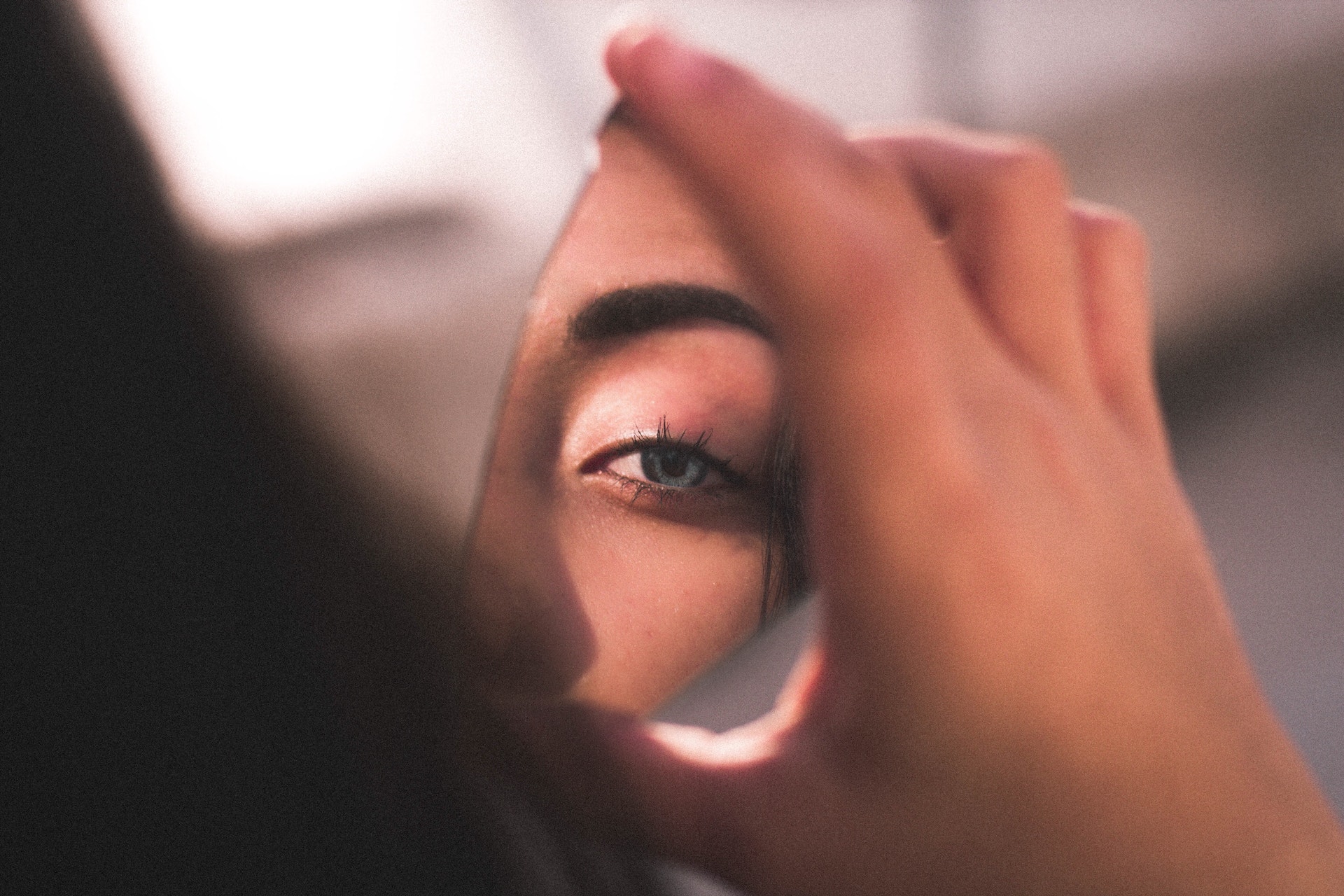 A dark-haired person's blue eye reflects in a shard of broken mirror.