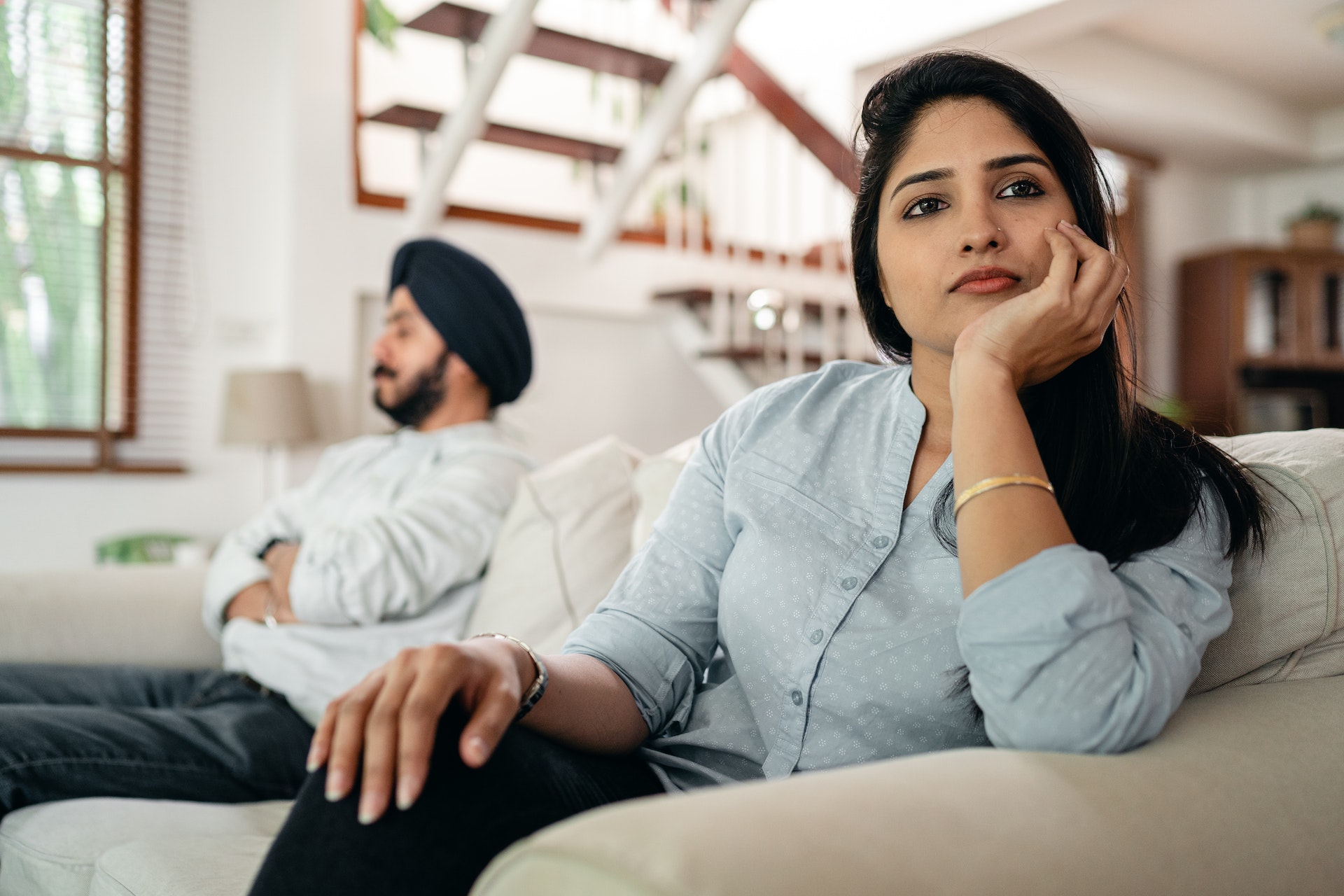 Two people sit far apart from one another on a couch, each deep in thought.