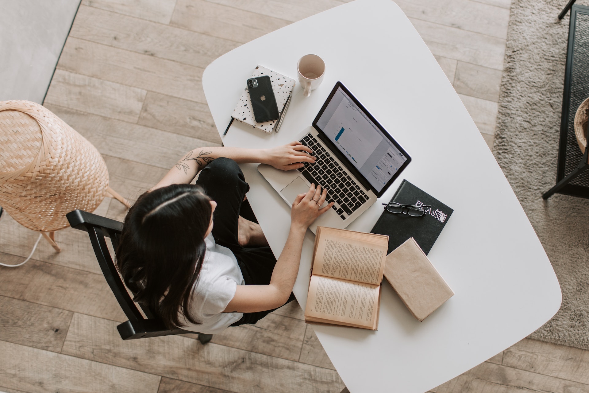 An overhead shot of a beta reader with long dark hair reading a book and typing on a laptop.