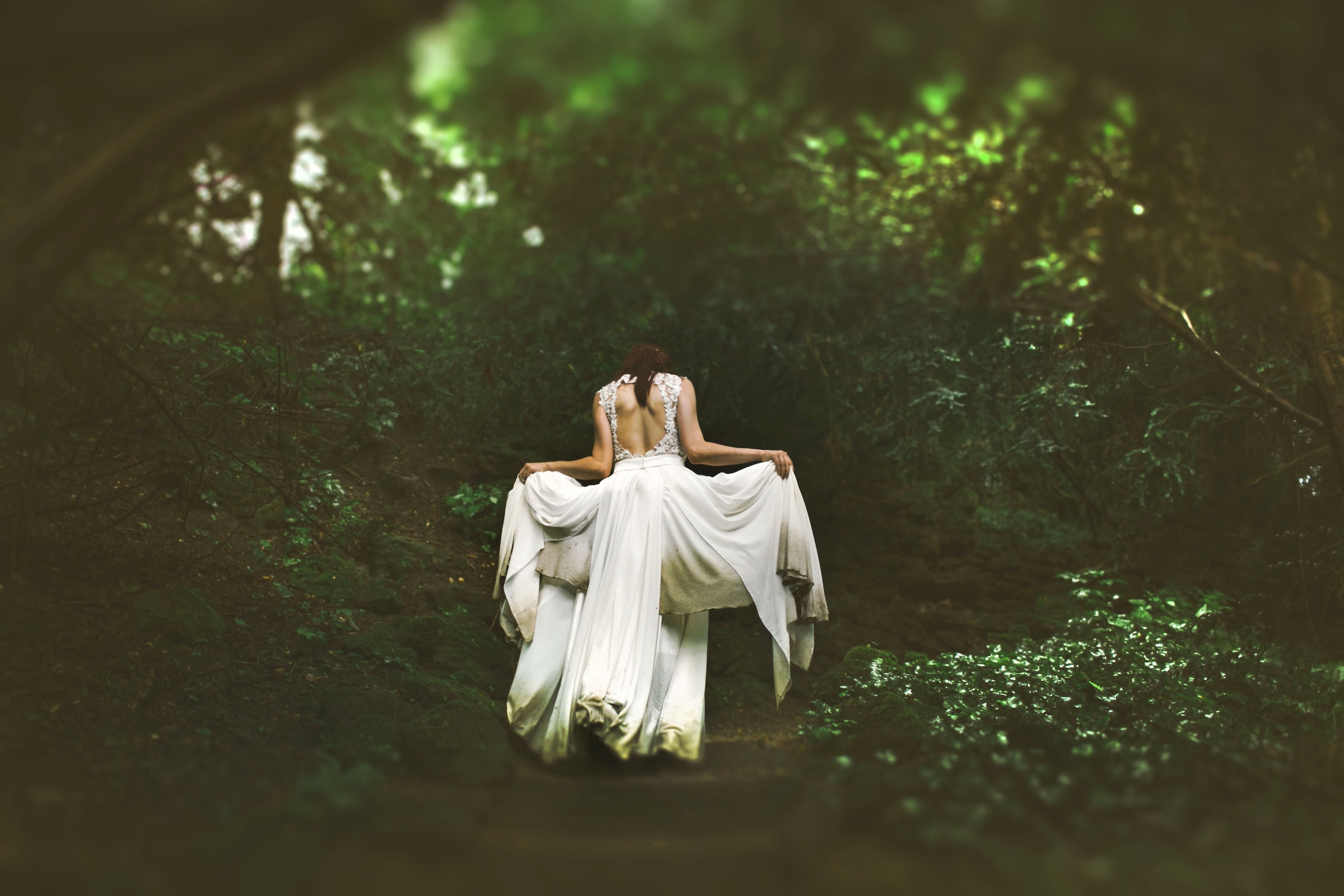 A person in flowy white dress walks through a blurry forest.