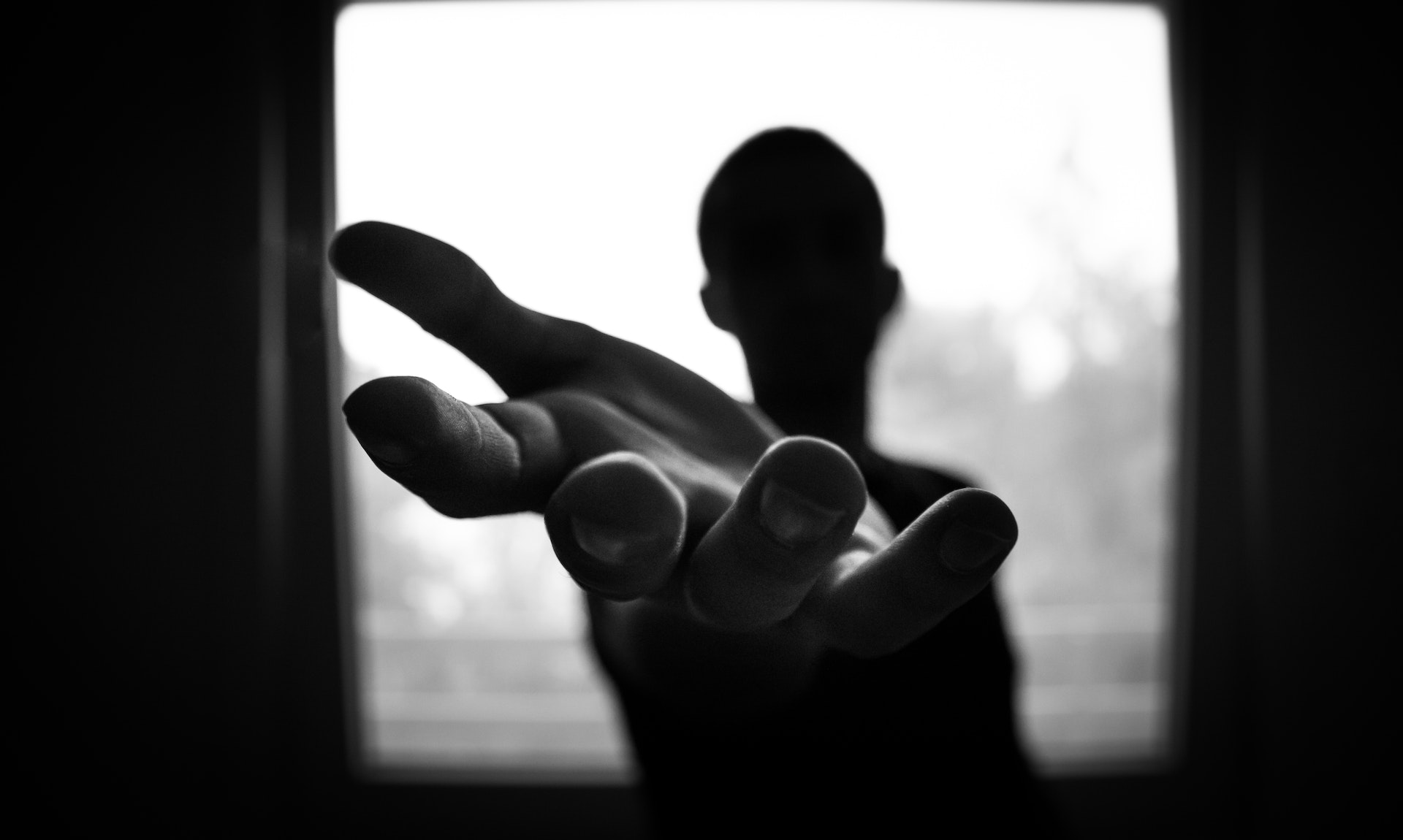 A shadowy figure reaches out a hand to the camera.