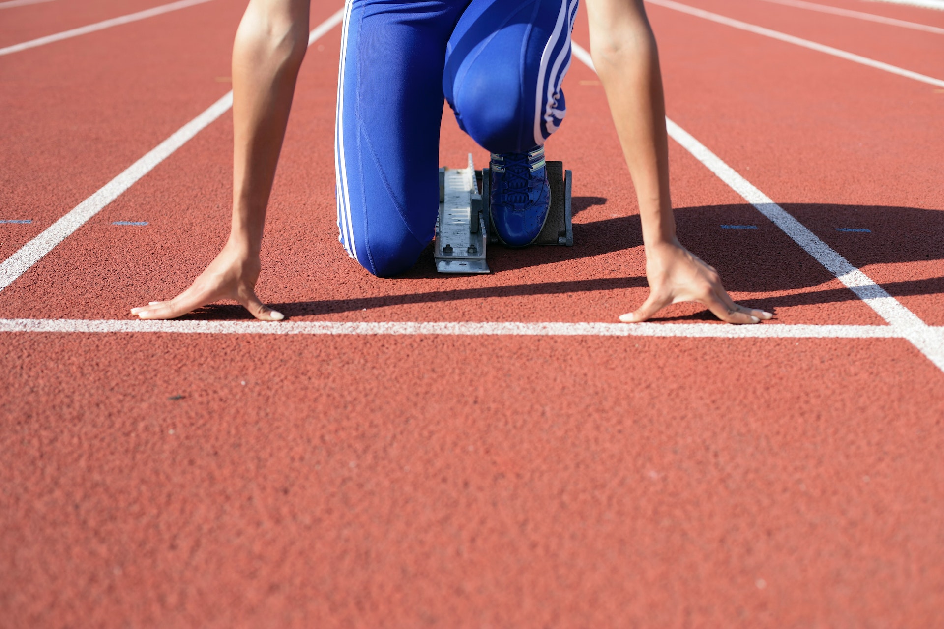 A runners hands and knees against the track as they begin to start a race.