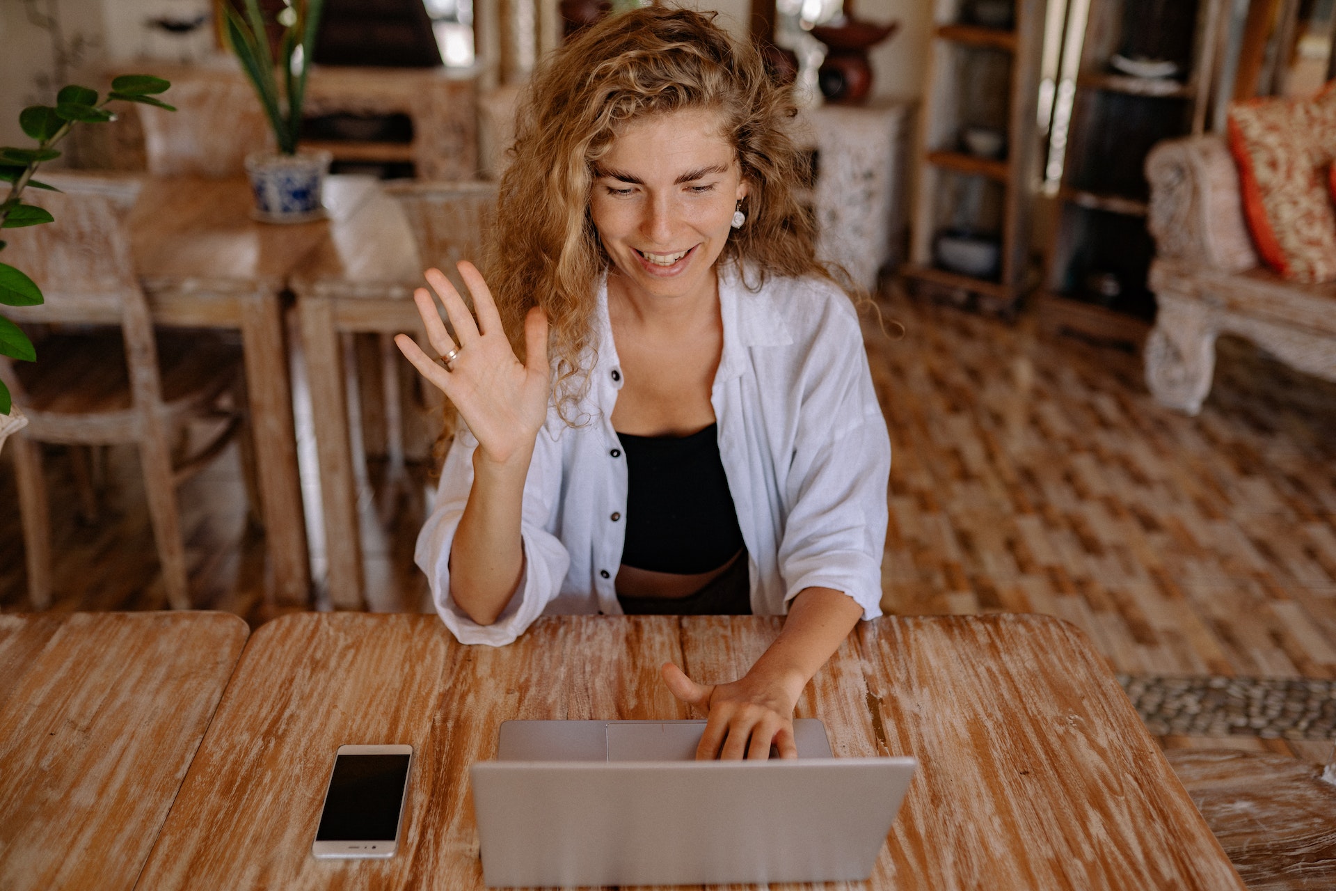 A writer in a cafe waves at a computer screen.
