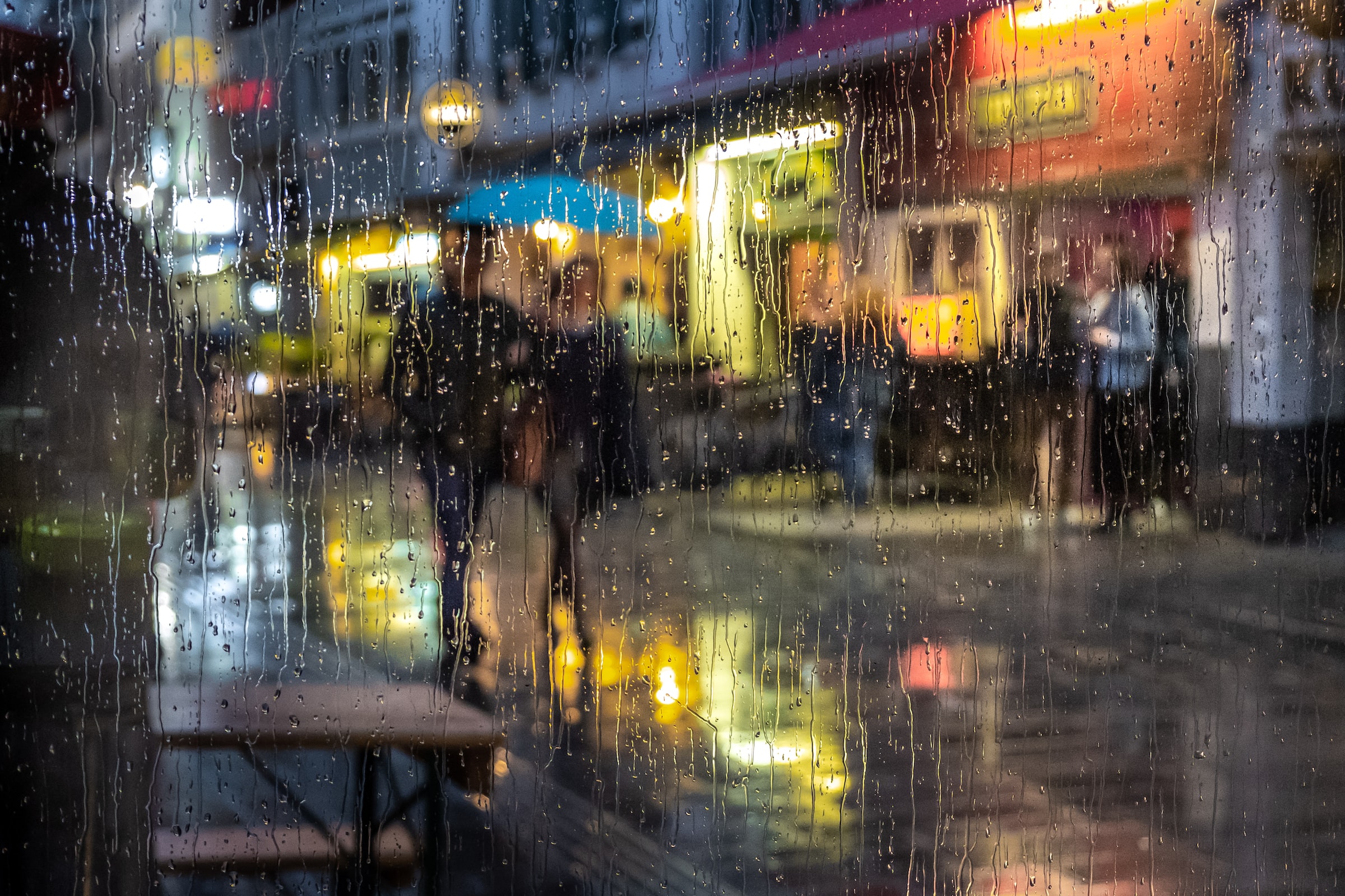 A view of two people walking down a city street through a rain-streaked window.