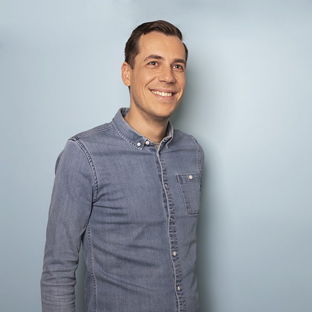 Mannelijke IT Trainee kijkt lachend in de camera bij een blauw achtergrond